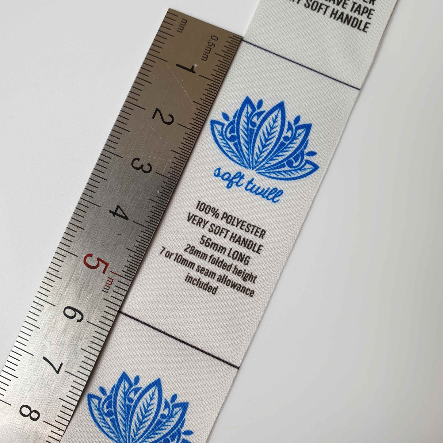 Textile label with blue floral design and measurement details next to a ruler on a white background